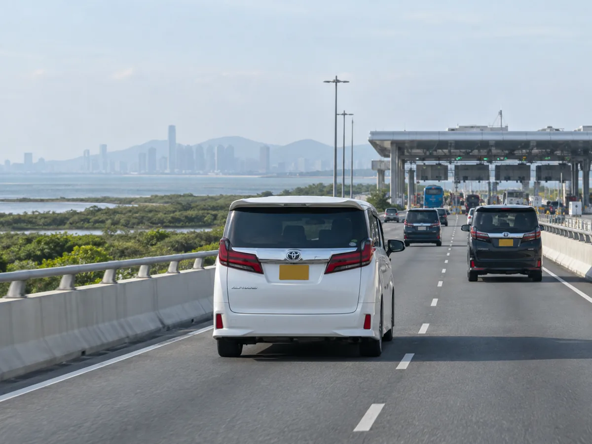 白色丰田埃尔法沿临水道路驶向口岸车道顶棚